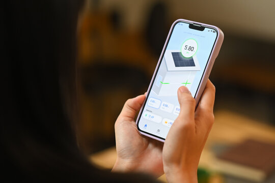 Woman holding a smartphone, displaying an app that monitors solar panel energy usage. Renewable energy systems concept