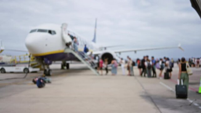 Blurry airplane with passengers boarding and deboarding on the tarmac, showcasing a crowded airport scene with people in the foreground and a commercial jet in the background, out of focus