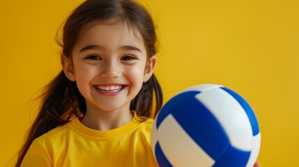 Smiling young girl in yellow holding a volleyball, set against a vibrant yellow background, expressing joy and energy.