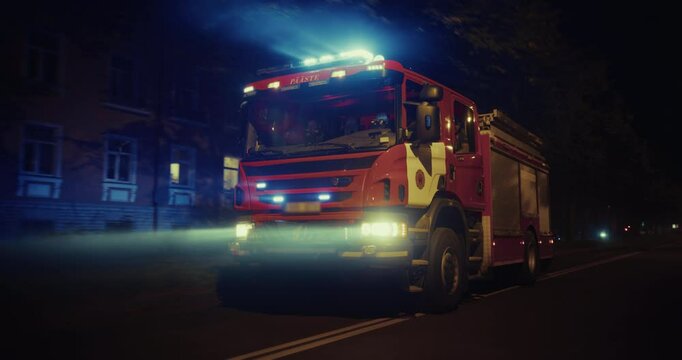 Emergency Lights Illuminate the Night as a Fire Truck Rolls Down a Street, Rushing to Assist in an Emergency. Truck with Firefighters Cuts Through the Night Traffic with Urgency. Car to Car Footage