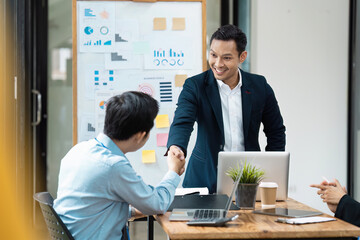 Business Professionals Shaking Hands in Modern Office During Meeting with Charts and Laptops