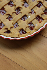 Tart with dark fig jam in a white ceramic cake pan on wooden table ready to be baked 