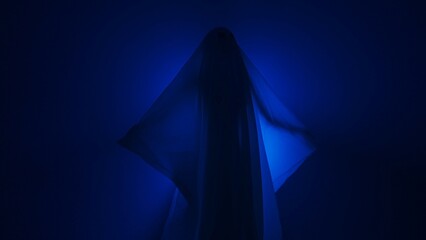 Funny Halloween ghost in white sheet makes scary gestures on background with blue spotlight in...