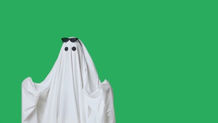 Funny halloween ghost in white sheet wears black glasses dancing coolly, isolated on chroma key green screen background. Happy halloween spooky concept.