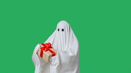 Funny halloween ghost in white sheet holding gift box, happy expression, isolated on chroma key green screen background. Happy halloween spooky concept.