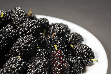 Fresh black mulberry on white plate on dark background. Concept of juicy and healthy seasonal...