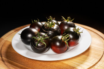 Ripe tomatoes in a white plate on a black background. Black tomatoes. Cumato tomatoes