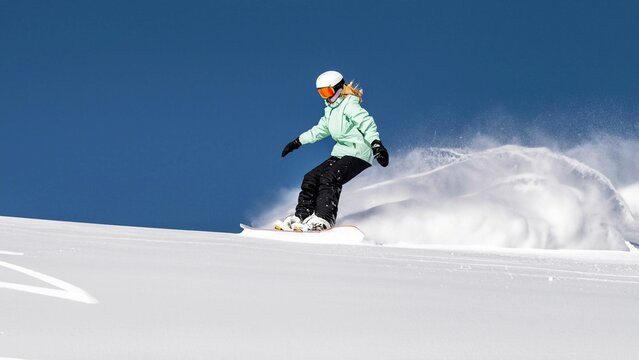 Snowboarder sliding down the hill. Snowboarder doing a toe side carve with deep blue sky in background. Young athletic snowboarder riding down on splitboard splashing snow. Skitouring freeride concept