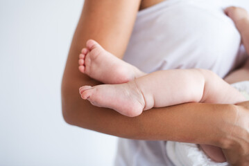 Close up. Small legs of the baby in the arms of the mother. Simple photo, white background.