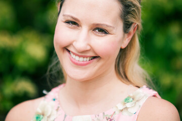 Portrait of happy young lady smiling at the camera with green summer time background 