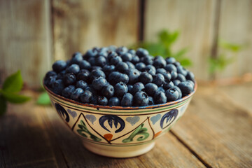 Blueberries in ceramic bowl on rustic wooden background. Selective focus. Shallow depth of field.