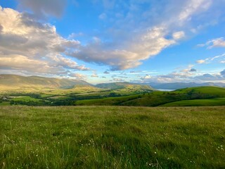 Obraz premium Expansive grassy meadow with distant hills and a bright blue sky with scattered clouds
