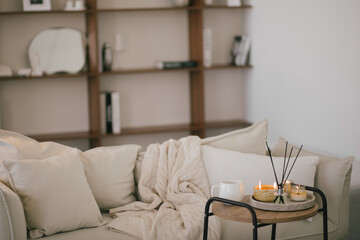 Still life with white mug, aromatic sticks and candles on a table in a cozy living room.