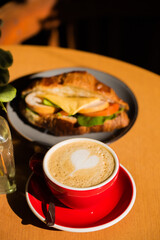 A sandwich with ham, lettuce, tomato, and cheese on a plate next to a cup of coffee on table in cafe