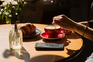 A person is sitting at a table with a cup of coffee and a croissant