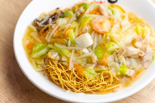 白い深皿に盛り付けられた、たっぷりの具材が食欲をそそる五目皿うどん。香ばしく揚げられたパリパリの細麺に、海老やイカ、豚肉、野菜の旨味が凝縮された熱々のあんかけが絡む。とろみのある餡の質感と彩り豊かな具材が映える、長崎名物や中華ランチの紹介に最適なクローズアップ素材。 | Nagasaki style Sara Udon with crispy noodles and seafood.