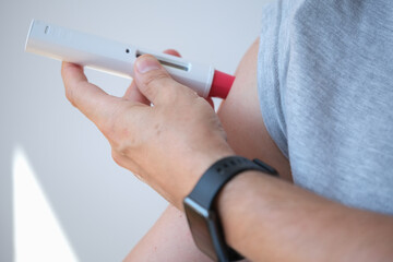 side close up of an anonymous person injecting himself a treatment such as insulin or Adalimumab,...