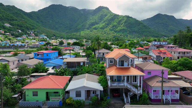 Colorful residential homes nestled in lush tropical hills, showcasing vibrant architecture. Surrounding neighborhood set against dramatic green mountain peaks. Aerial view.​