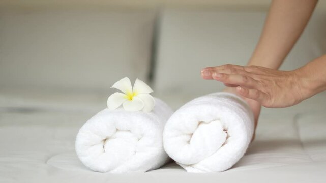 A hotel maid stacked towels on the bed and placed flowers on the towels in a hotel room.