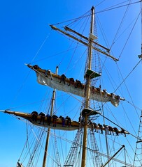 A majestic tall ship with crew members scaling its masts, set against a vibrant blue sky, showcasing the timeless beauty of maritime history.