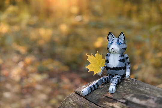 autumn nature background.  cute wooden cat toy with yellow maple leaf in forest. fall season. copy space