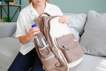 The girl puts a bottle of water in her school backpack.