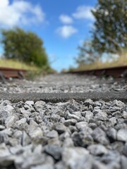 Close-up view of old railway tracks with scattered stones, leading into a vibrant landscape under a bright blue sky.