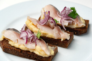 Open-faced sandwiches with herring and onions served on a white plate