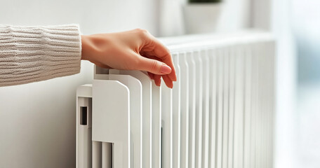 Hand touching white radiator for warmth in home interior. Winter heating and energy saving concept