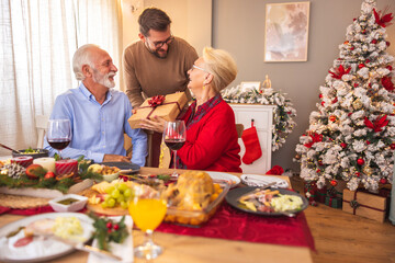 Parents exchanging Christmas presents with son over dinner at home