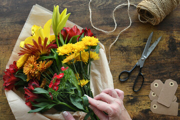 Female hands arranging colorful autumn flowers bouquet table - high angle overhead view flat lay