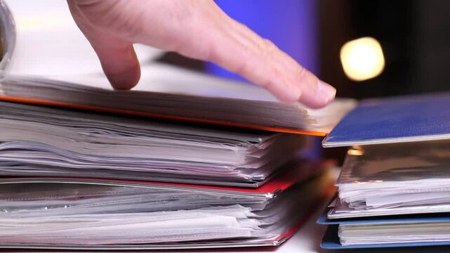 close-up man's hand leafing through documents in a orange, red, blue folders