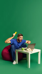 Emotional young man looking on laptop, holding credit card and expressing excitement against green background. Betting, successful deals. Concept of shopping, sales, Black Friday, Cyber Monday