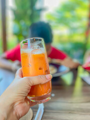 Closeup of glass of vibrant orange thai tea iced drink in a women hand with blurry backgrouhnd , relaxed atmosphere in a cafe or restaurant, enjoy a moment of refreshment., vertical color image.