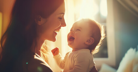 A mother holding the newborn in front of a bright light from a window at home. Close up photo of a happy woman and laughing child looking at each other with love and care, in a warm atmosphere.