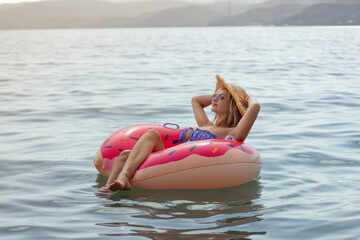Beautiful young woman with inflatable donut in blue sea 