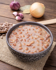 Cooked brown beans in a bowl over wooden table with onion and garlic