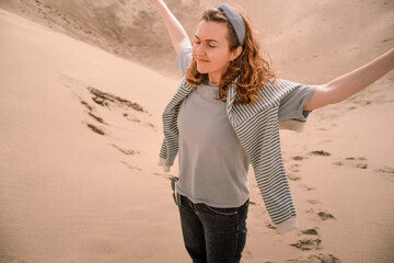 young woman with wavy hair in grey t-shirt and sweater draped over shoulders enjoying sun and...