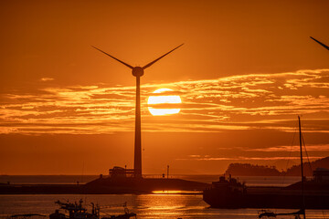 A view of the sunset on the beach with a view of wind turbines that generate electricity

