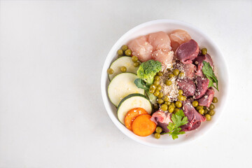 BARF (Biologically Appropriate Raw Food) food concept, Healthy bowl for domestic pets background with cat cute tabby kitten paws in pic.  Portion of raw meat, chicken, fish, vegetables, oats