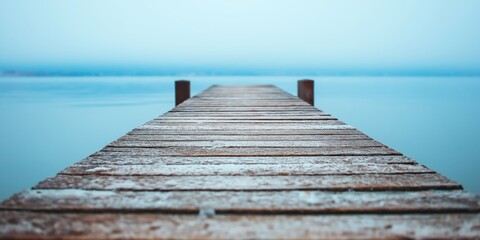 Fototapeta premium A serene wooden dock covered in frost stretching out into a calm and misty body of water, evoking stillness and solitude.
