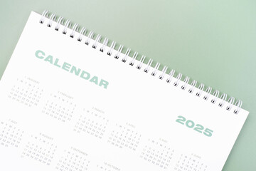 White calendar 2025 on green background close-up, planning concept.