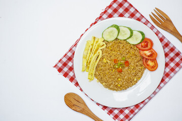 A plate of delicious fried rice served with sliced cucumber, tomato, and egg strips, placed on a red checkered cloth. photographed from a top angle