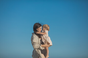 Smiling mother and beautiful daughter having fun on the beach. Portrait of kid embracing her mom during summer.