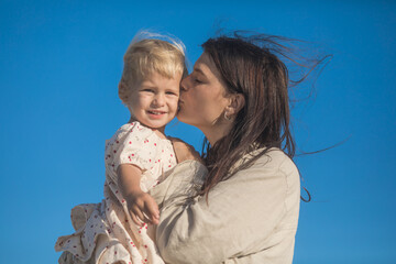 Smiling mother and beautiful daughter having fun on the beach. Portrait of kid embracing her mom during summer.