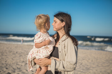 Smiling mother and beautiful daughter having fun on the beach. Portrait of kid embracing her mom during summer.