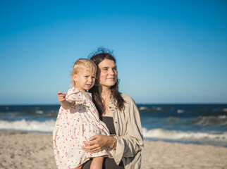 Smiling mother and beautiful daughter having fun on the beach. Portrait of kid embracing her mom during summer.