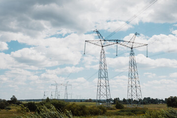 High voltage pylons against the blue sky with white clouds and bright green meadow. Power lines stretching into the distance. Perspective. Electricity