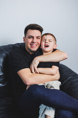 Happy dad hugs his little son while sitting on sofa. A father's love for his son. Family relations...