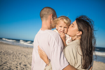Obraz premium Happy family at the ocean. Parents kiss her daughter